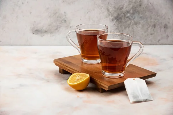 A cup of garcinia cambogia tea with a tea bag and sliced lemon on a wooden table, illustrating the proper dosage and usage.