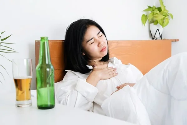 Image of a fatigued person drinking a glass of alcohol, relevant to the blog post titled 'Understanding the Risks: Melatonin and Alcohol in 2023' by PatchMD - Vitamin Patches and Supplements.