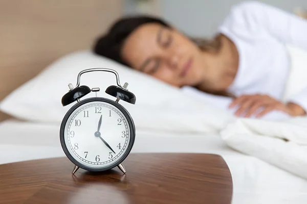 Image of a person peacefully sleeping in a comfortable bed with a clock in the background, relevant to the blog post titled 'Is Melatonin Addictive: Exploring the Benefits, Side Effects, and Risks in 2023' by PatchMD - Vitamin Patches and Supplements.