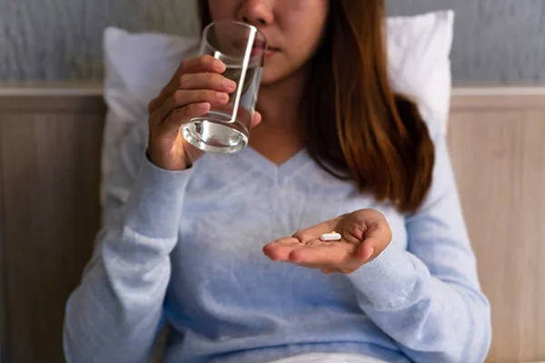 Image of a person taking a melatonin supplement while holding a glass of water, relevant to the blog post titled 'Understanding the Risks: Melatonin and Alcohol in 2023' by PatchMD - Vitamin Patches and Supplements.