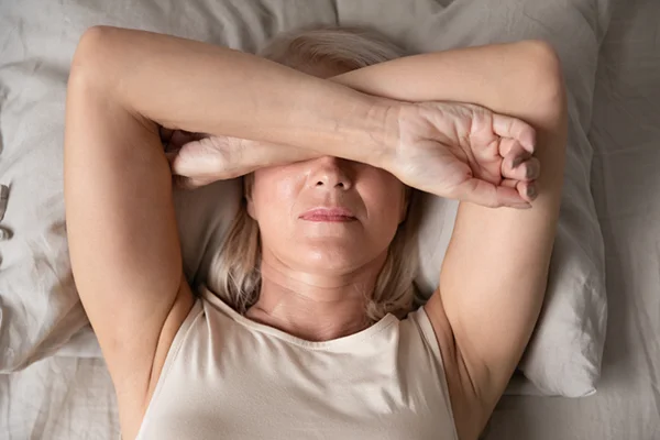 Image featured in the 'What Are the 34 Symptoms of Menopause: What You Need To Know' post for PatchMD - Vitamin Patches and Supplements, portraying a woman in her 50s experiencing night sweats and hot flashes