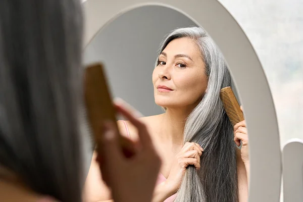 Image for 'How to Reverse Thinning Hair After Menopause - An Expert Guide' post by PatchMD - Vitamin Patches and Supplements, featuring a woman with vibrant, healthy hair gazing at her reflection in the mirror.