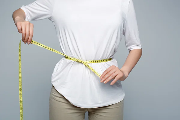 Visual representation for the 'Conquer Menopause Belly: Strategies for Losing Weight and Slimming Your Mid-Section' post by PatchMD - Vitamin Patches and Supplements. Depicts a woman measuring her waist to track her menopause belly fat, highlighting the focus of the article on addressing this specific concern during menopause.